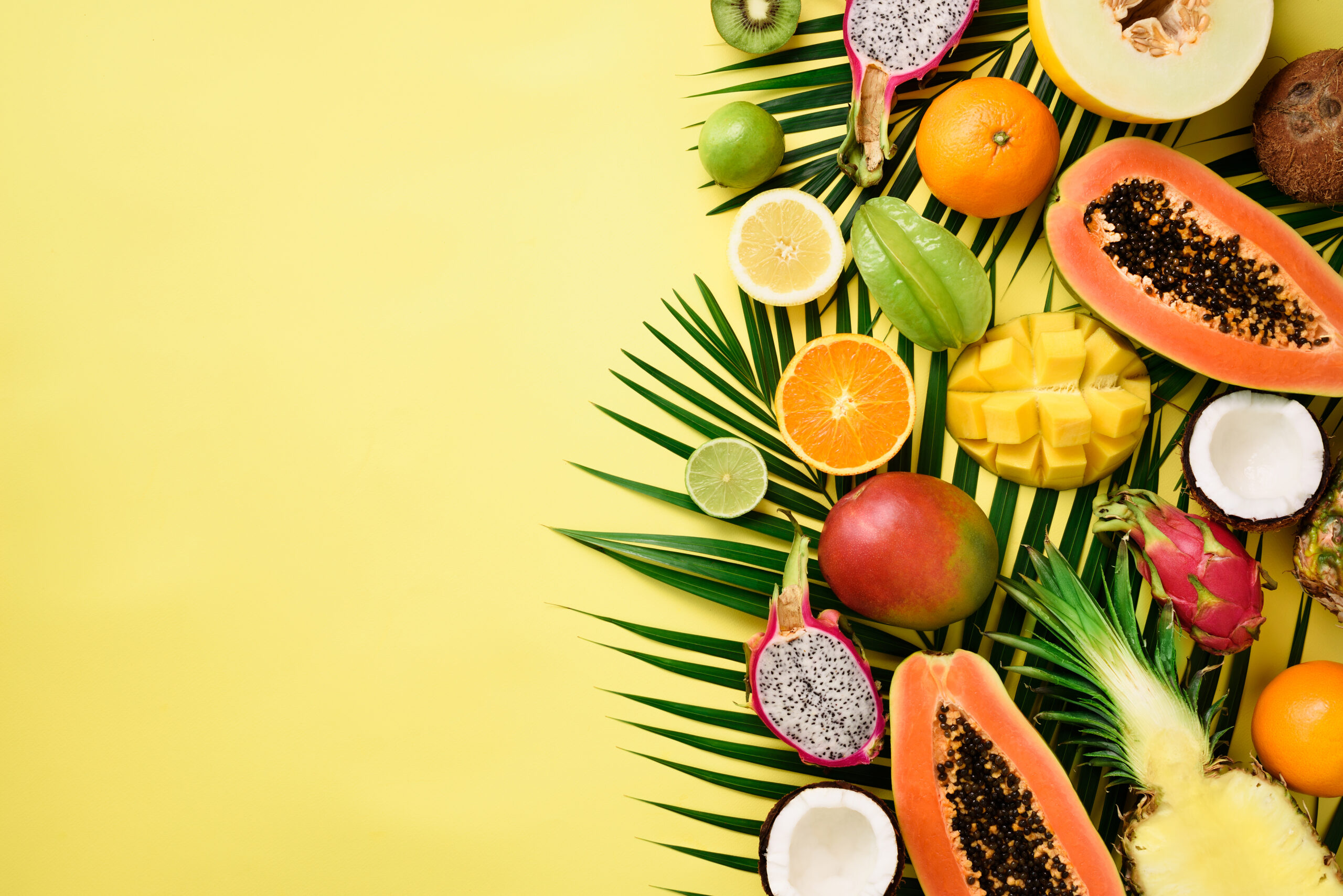 Exotic fruits and tropical palm leaves on pastel yellow background - papaya, mango, pineapple, banana, carambola, dragon fruit, kiwi, lemon, orange, melon, coconut, lime. Top view